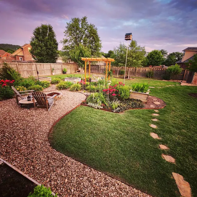 A deep-green lawn curving past a fire-pit patio under a purple dusk sky
