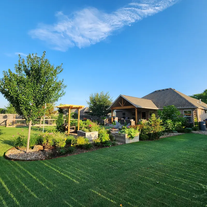 A freshly striped backyard lawn beside planted island beds and a cedar pergola under a clear blue sky