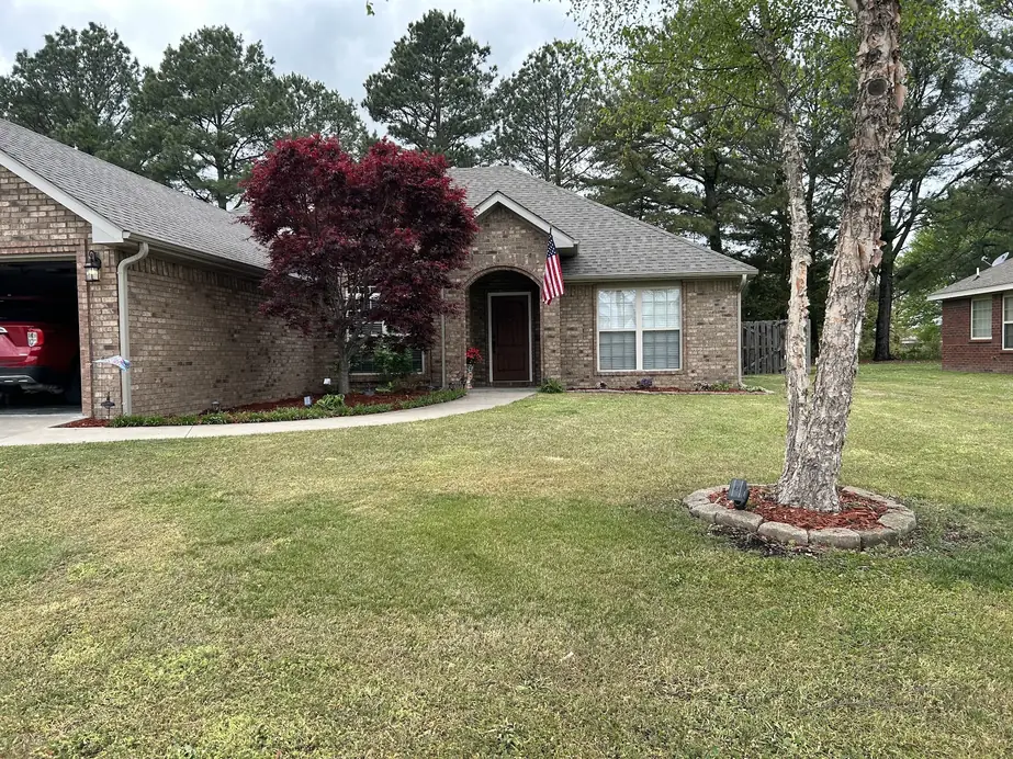 Front lawn of a brick home with a red Japanese maple and fresh mulch beds in Northwest Arkansas