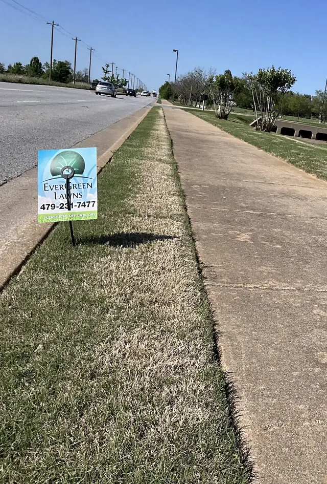 An EverGreen Lawns flag reading please stay off until dry, planted in a treated roadside strip